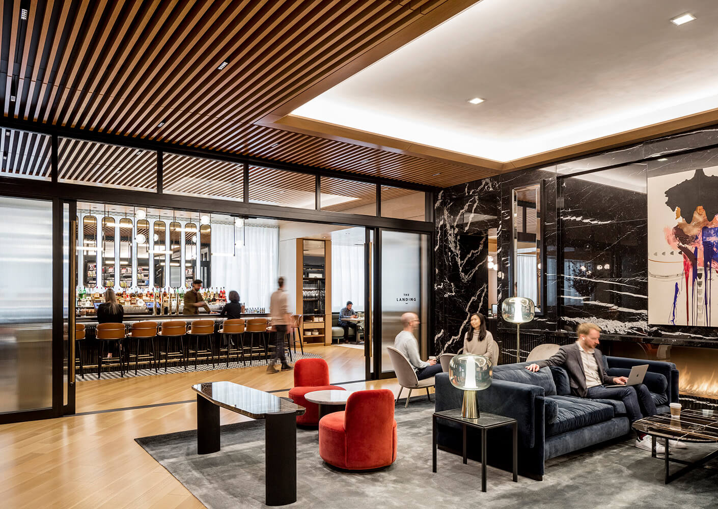 Interior of a hospitality space with a bar area and lounge seating. Guests engage in conversation and work at tables, featuring elegant design elements.