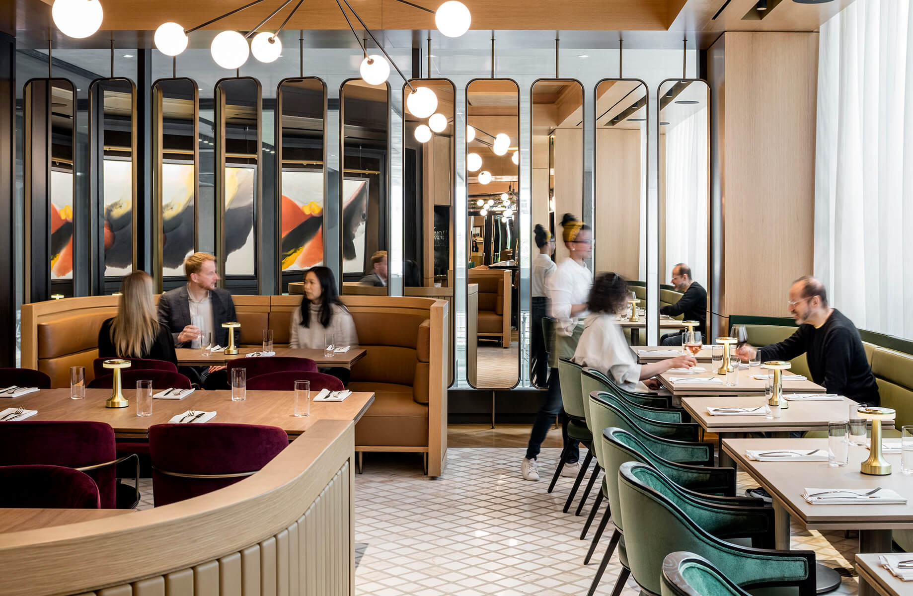 Interior of a stylish restaurant featuring seating areas with booths, tables, and decorative lighting. Guests engage and staff serve meals.