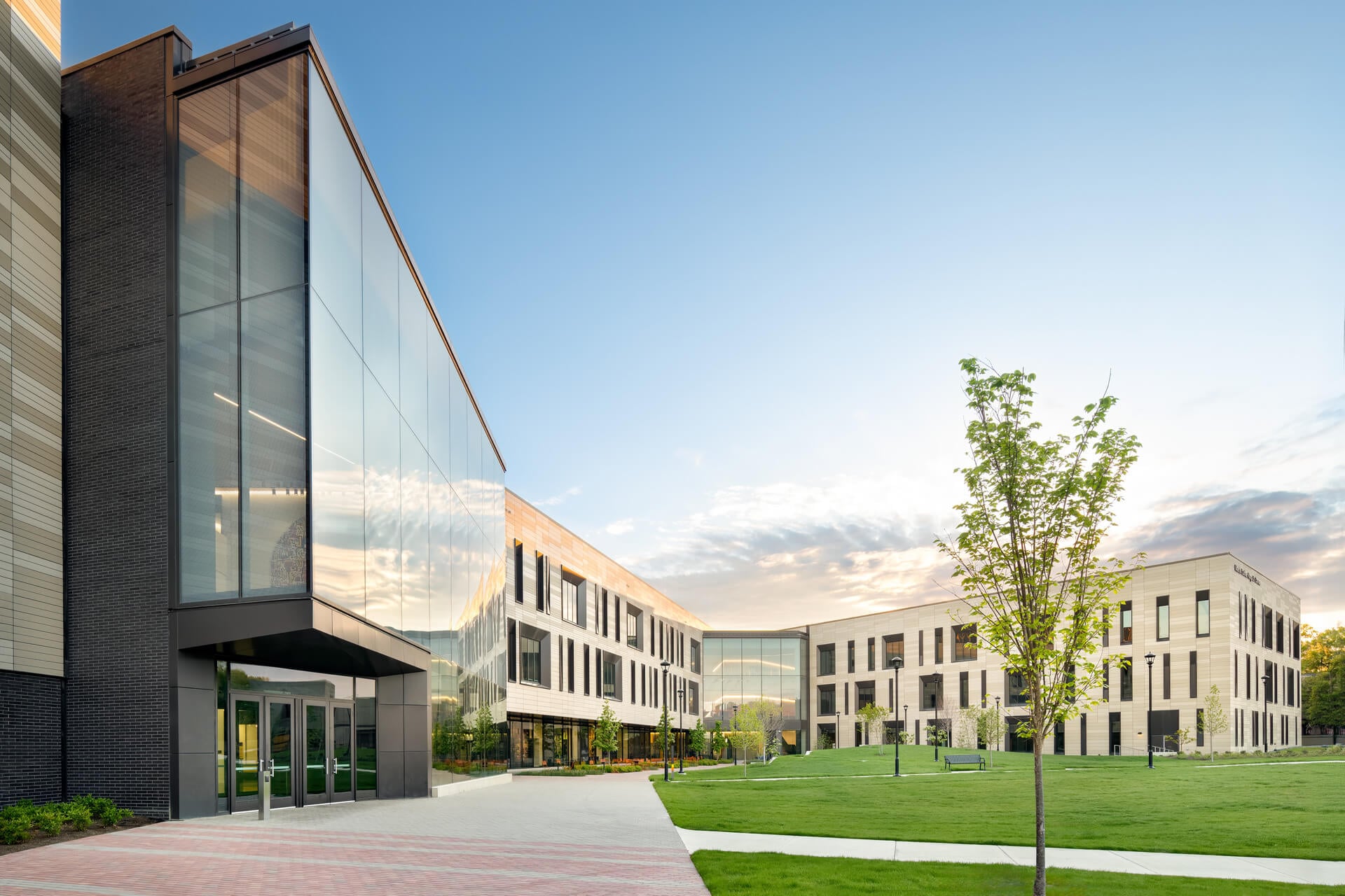 Exterior view of a glass and stone building complex featuring landscaped green spaces and modern architecture against a clear sky.