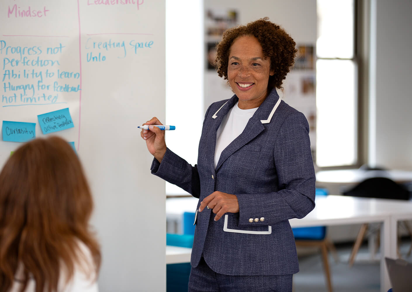 Business professional presenting ideas at a whiteboard, with notes on mindset and leadership concepts, engaging with a colleague.