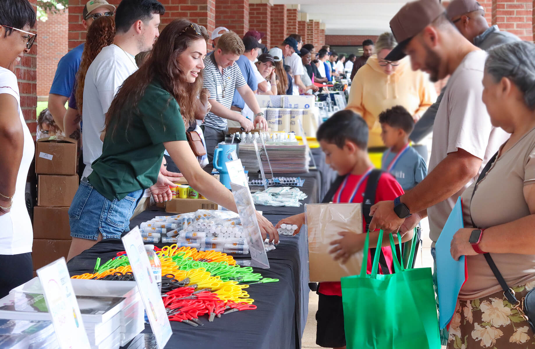 Community event featuring people engaging at tables with school supplies and other items, showcasing interaction and participation.