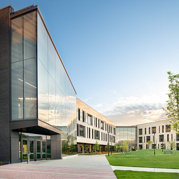 Contemporary office building with large glass windows, landscaped grounds, and a clear sky, showcasing a blend of architecture and nature.