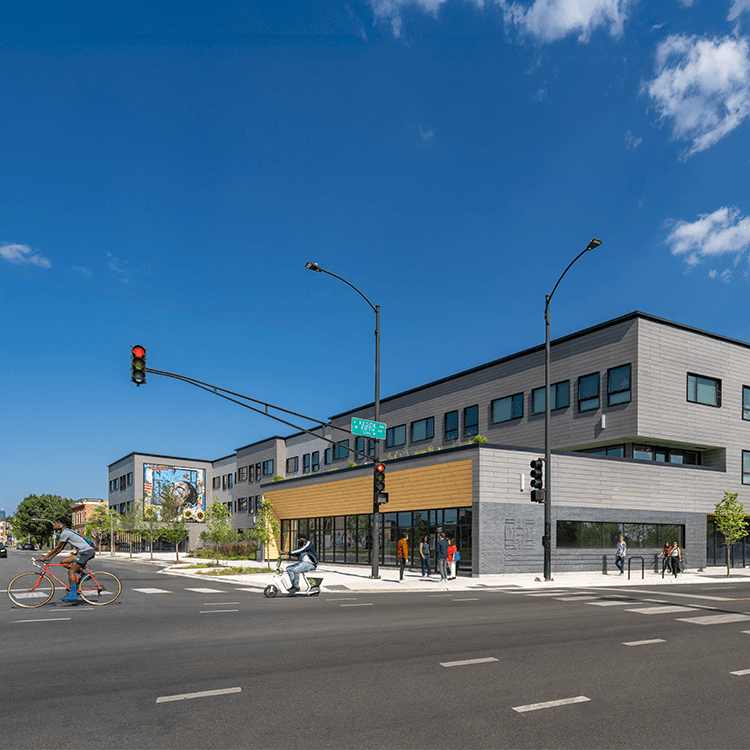 New urban building at an intersection featuring a mixed-use design, cyclists, pedestrians, and clear blue skies in the background.
