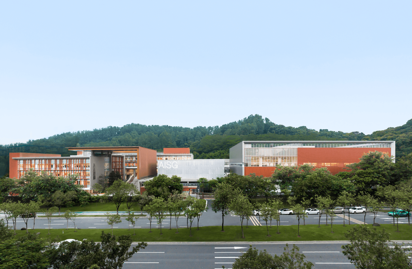architectural building with greenery, showcasing multiple structures and a landscaped entry along a tree-lined avenue.