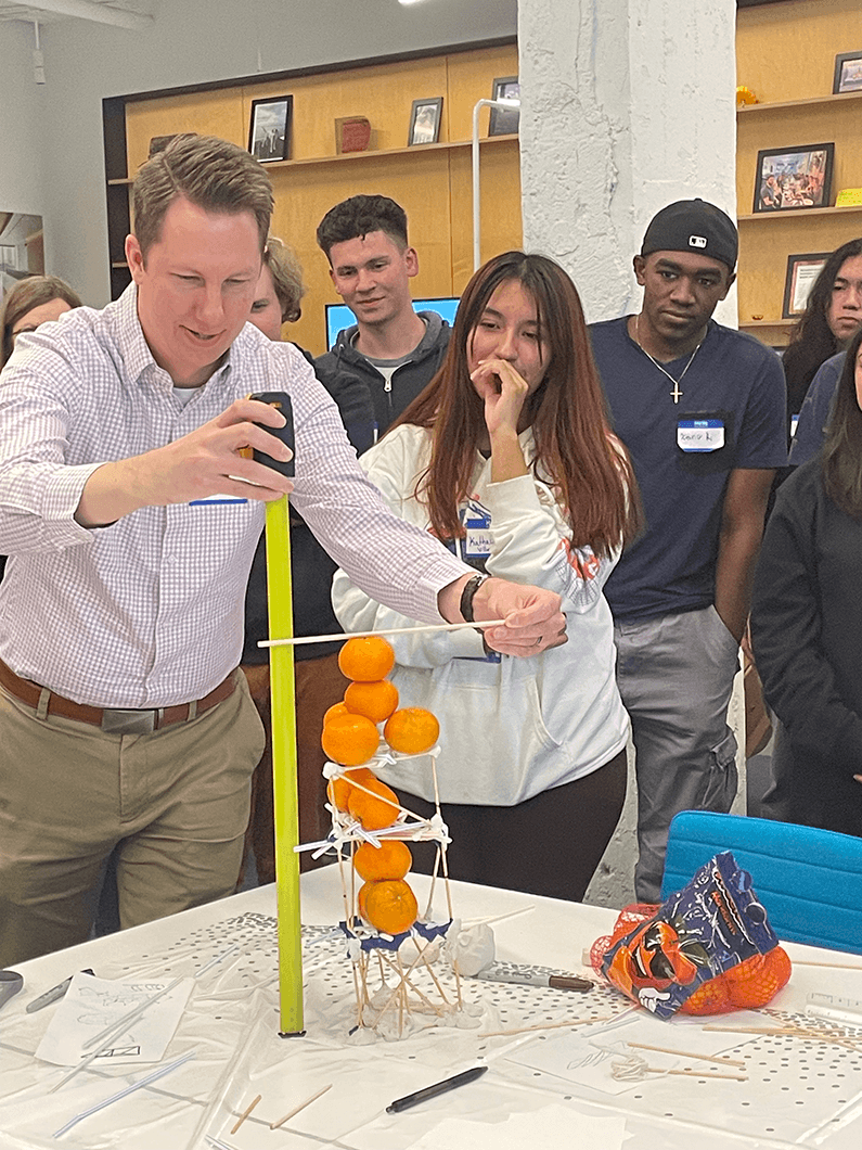 Participants compete in a structural engineering challenge, building a tower with oranges, using measuring tools and materials in a collaborative environment.