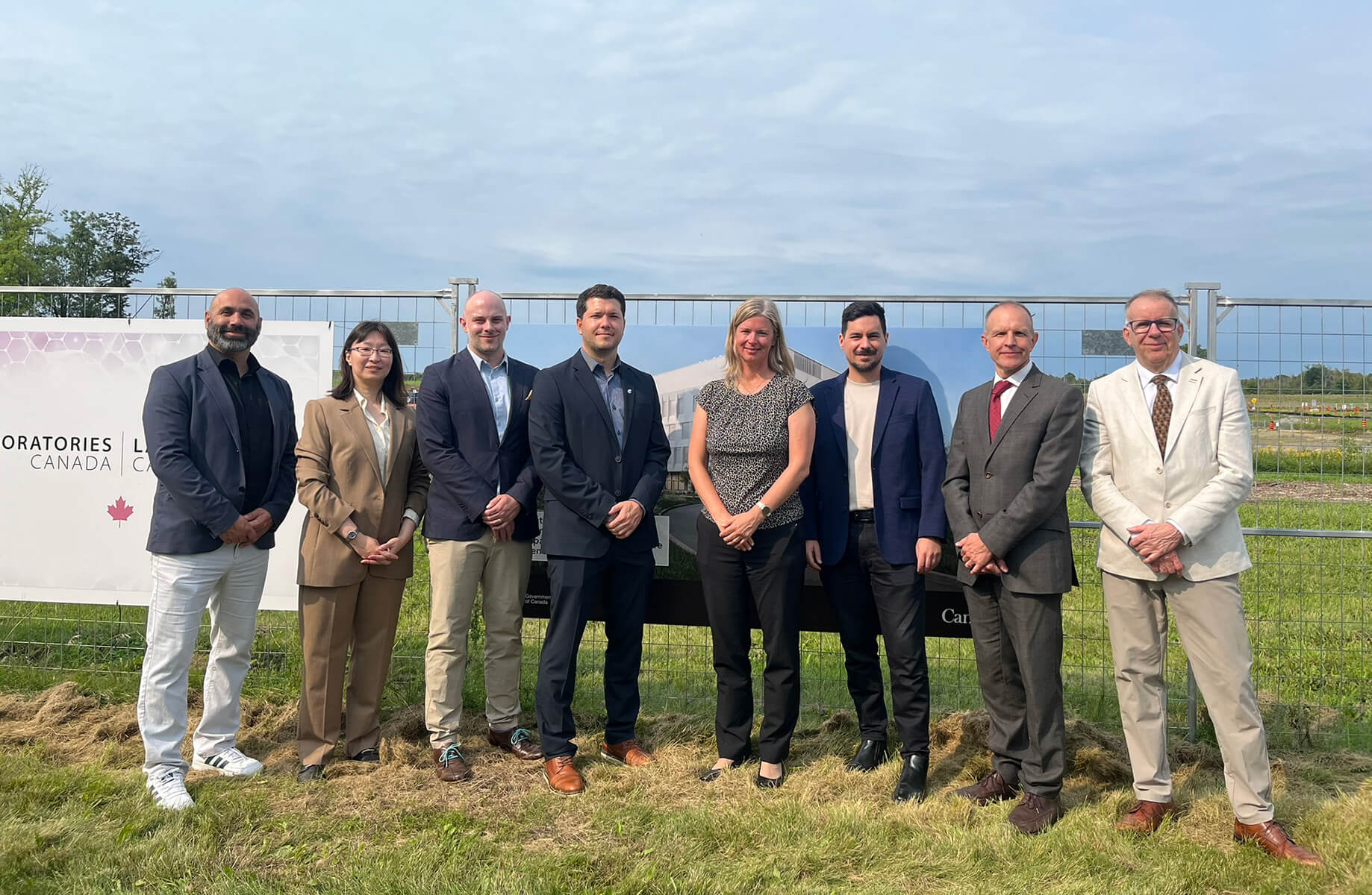 Group of professionals at a groundbreaking ceremony for laboratories in Canada, standing in front of a promotional sign and construction site.