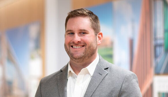 Smiling man in a gray blazer poses in front of architectural images, highlighting his professional environment.