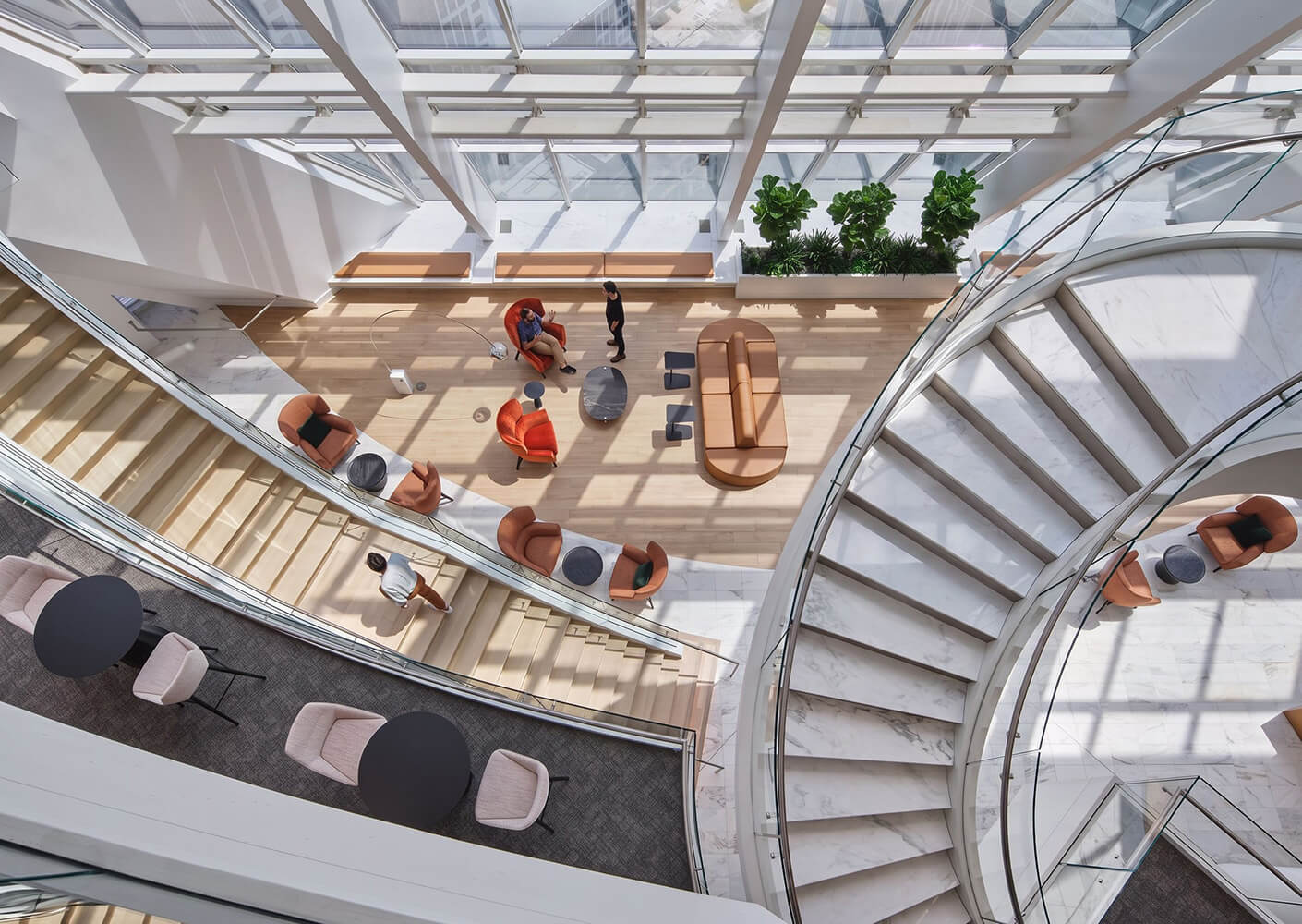 Interior view of a stylish space featuring a staircase, seating areas, and greenery, designed for collaboration and relaxation. Natural light fills the area.
