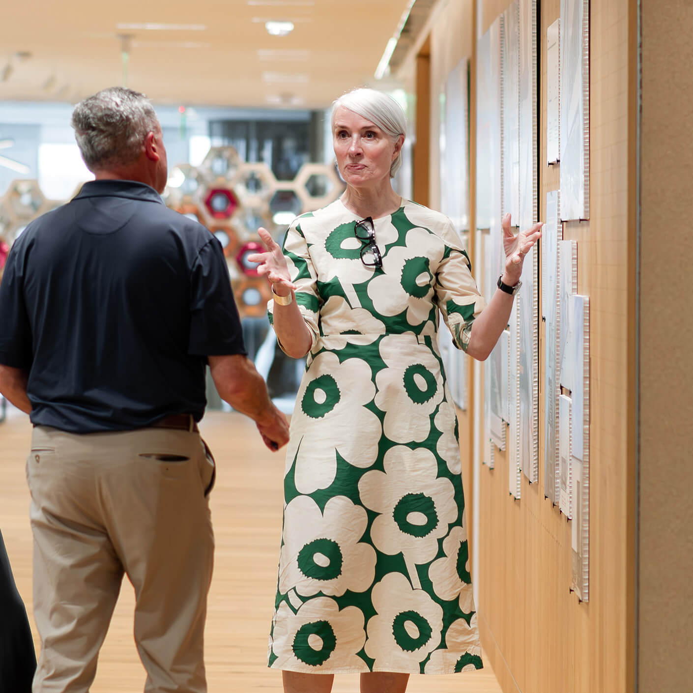 Robin Osler gestures while speaking to a man in Perkins&Will's Boston studio with artwork and wooden flooring.