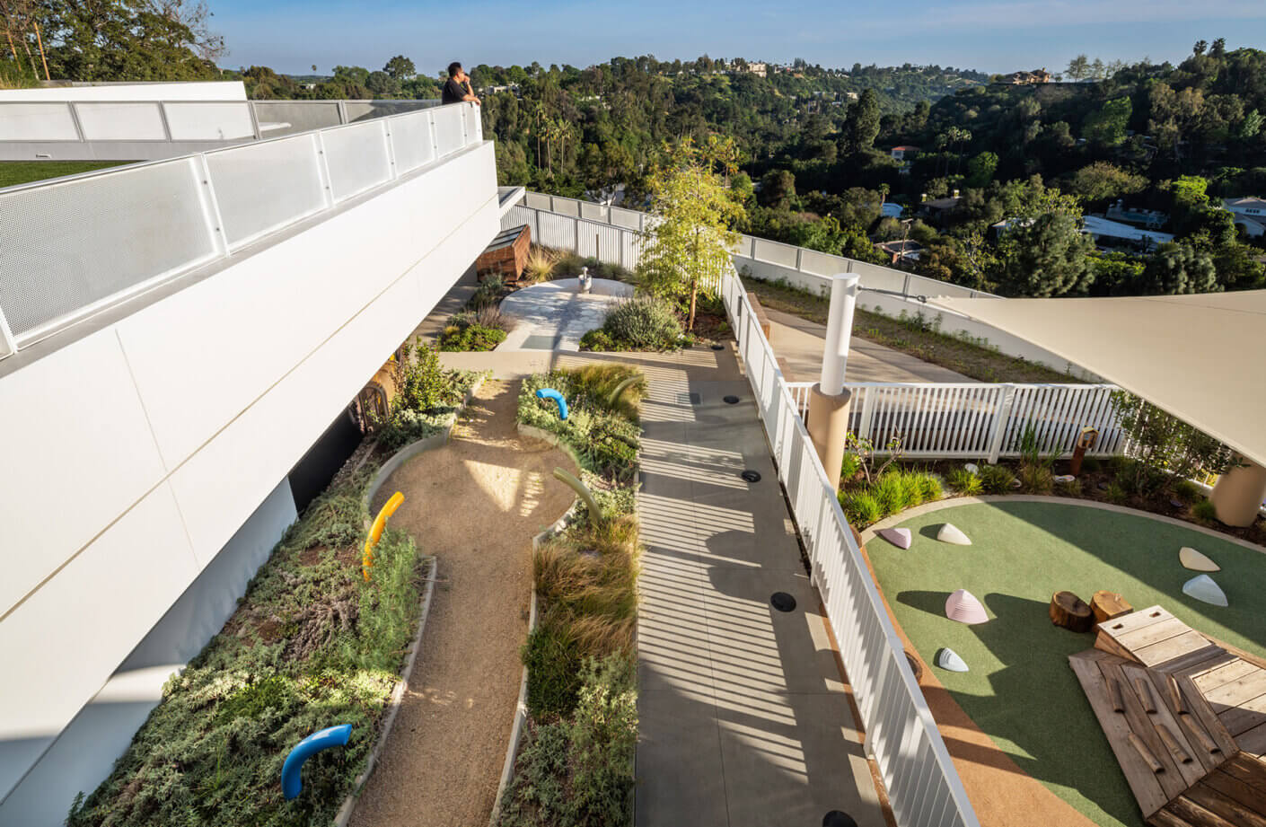 Aerial view of a landscaped outdoor area featuring pathways, grassy play zones, and seating in a residential setting. Man overlooks the space from above.