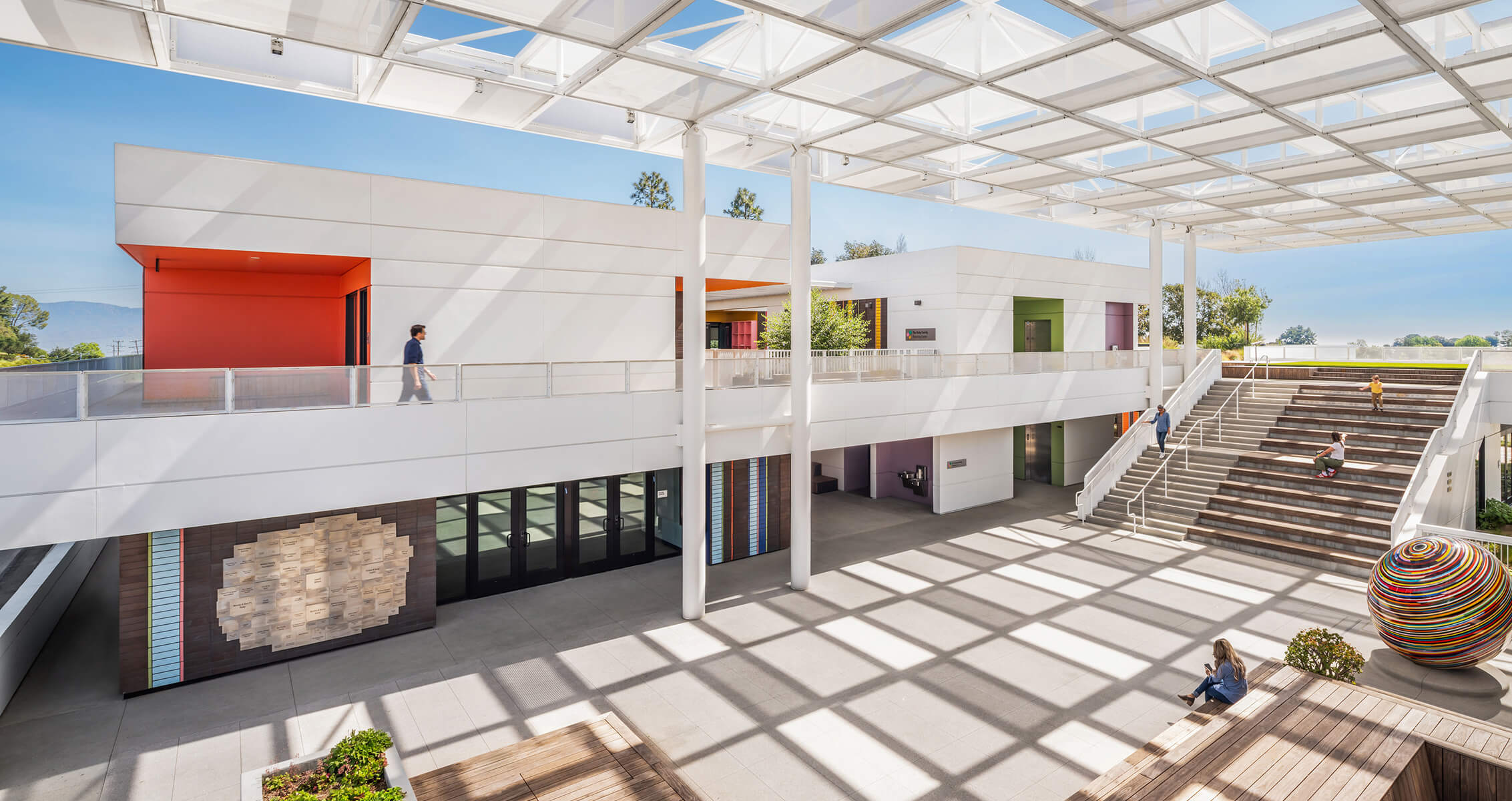 A spacious architectural interior featuring multiple levels, diverse colors, open walkways, and seating areas under a large, translucent canopy.