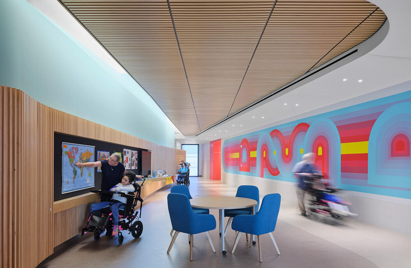 Interior view of a vibrant school space featuring a colorful mural, wooden accents, seating area, and individuals engaged in activities.