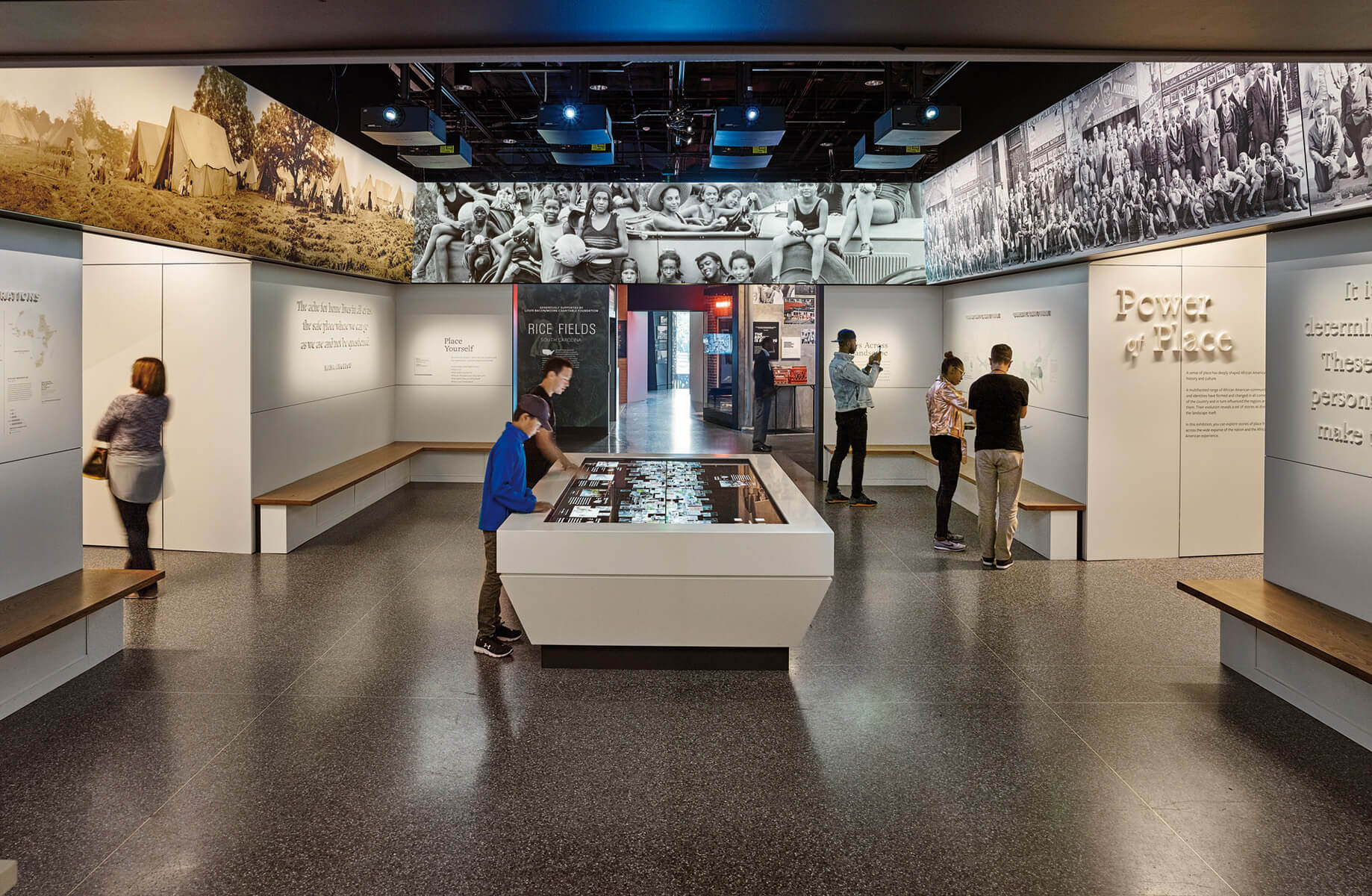 Exhibit space featuring interactive displays, historical images, and visitors engaging with educational content on community and history.