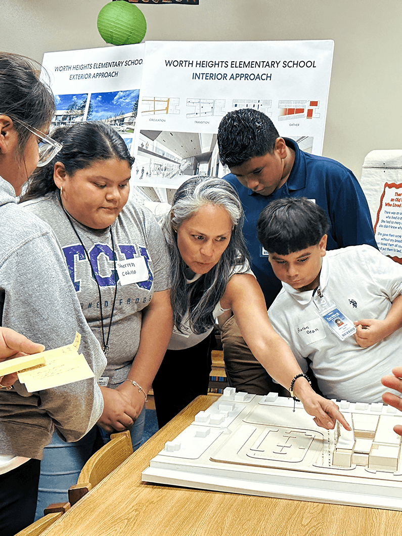 Students and an instructor discuss a scale model of Worth Heights Elementary School, focusing on design elements and layout options.