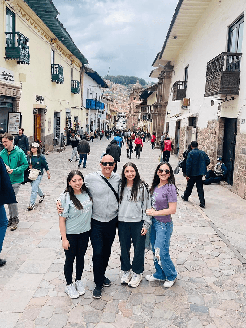 Family posing together on a busy street in Cusco, Peru, with shops, pedestrians, and historic buildings in the background.
