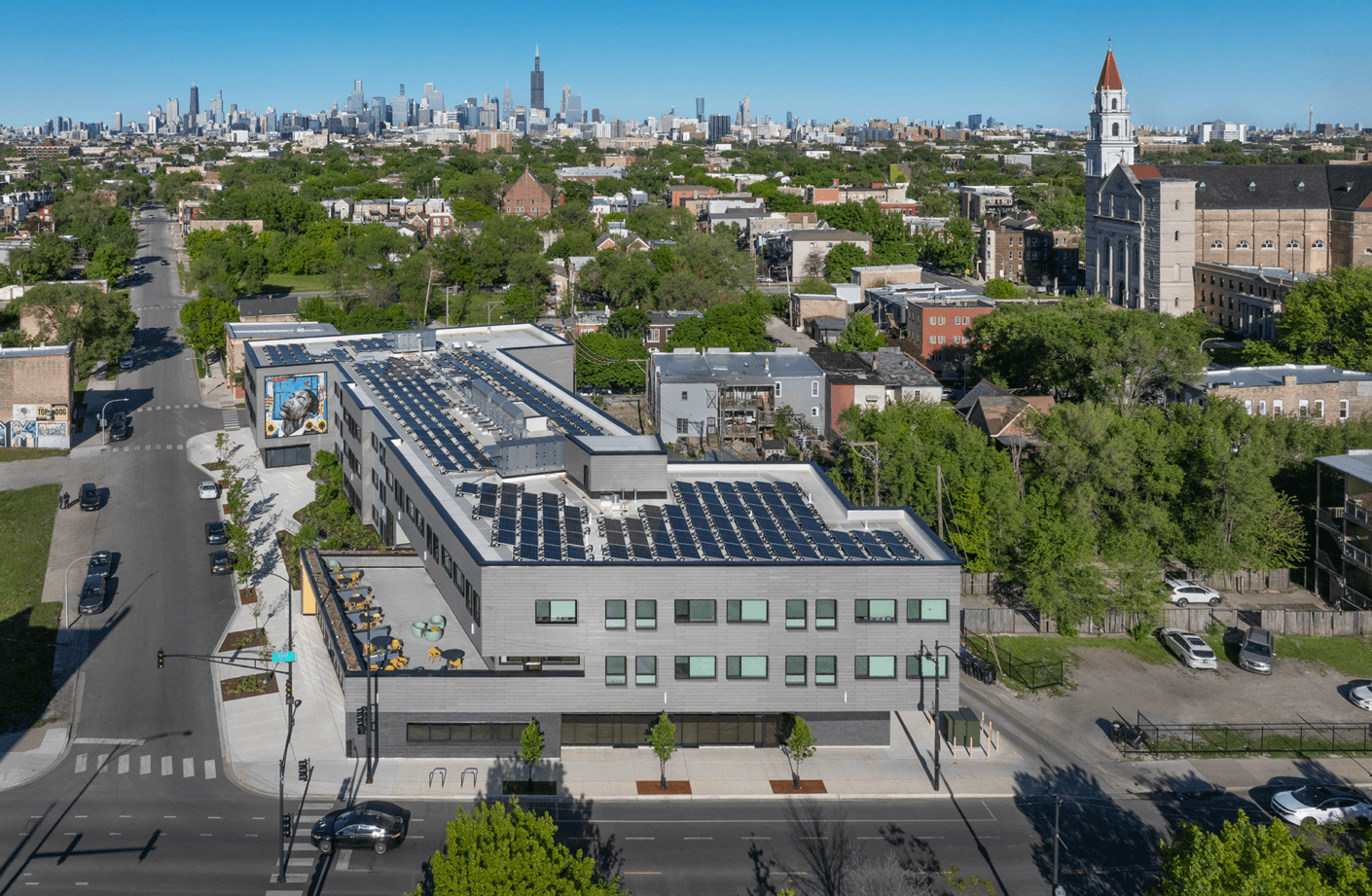 Aerial view of a building with solar panels on the roof, surrounded by green trees and Chicago’s skyline in the background.