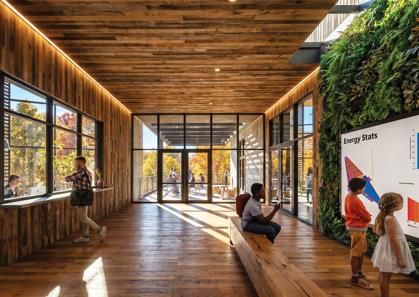 A spacious interior with wooden walls and floors. People engage with a digital display on energy stats while enjoying views of fall foliage outside.