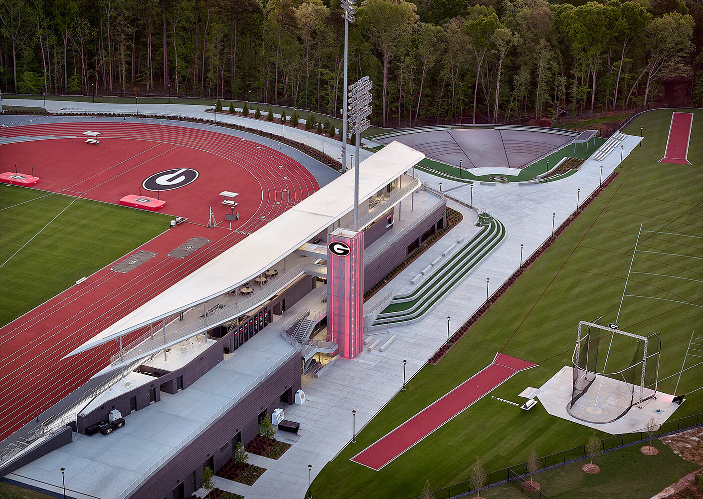 Aerial view of a university athletic facility featuring running tracks, a green field, and a spacious building with seating and lighting.
