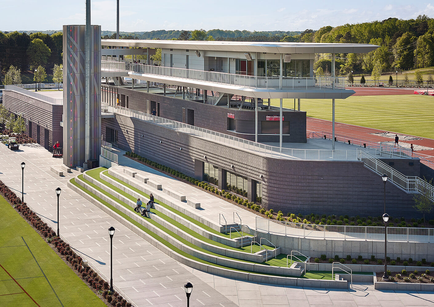 Sports facility with tiered seating, a patio area, and a multi-level building featuring large windows and a modern structure.