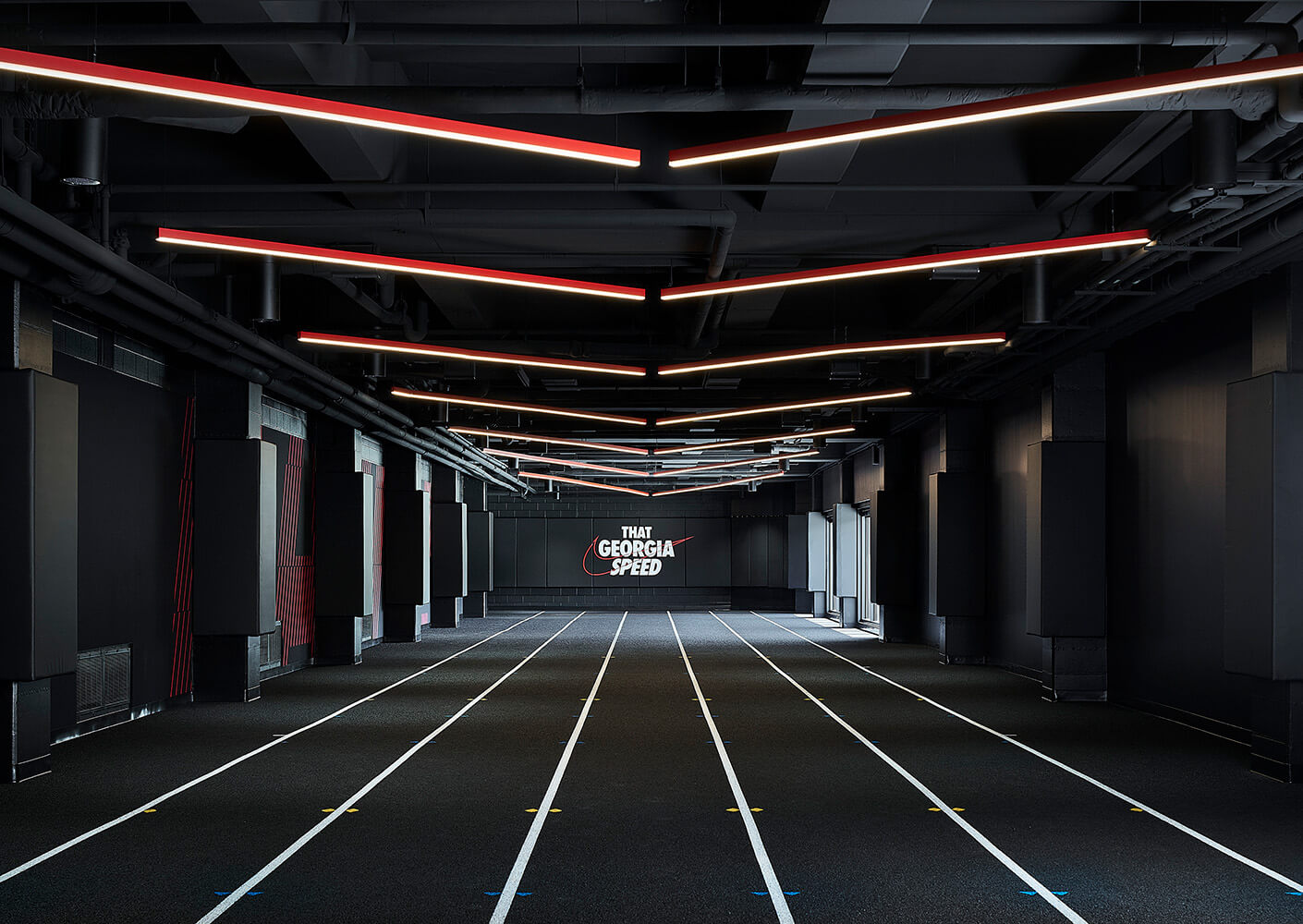 Indoor athletic facility featuring track lanes, black walls, and ceiling lights in a zigzag pattern, with a That Georgia Speed sign on the wall.