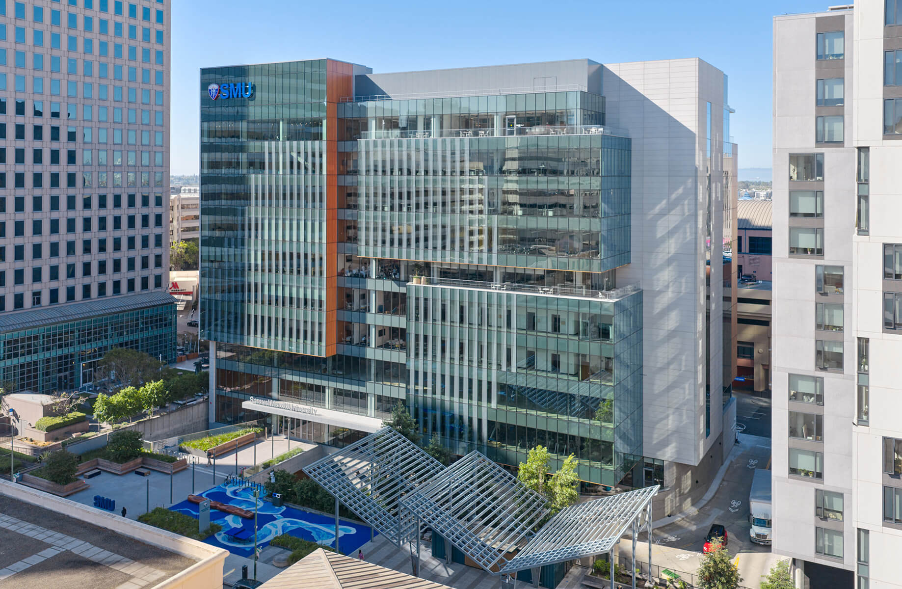 Glass and concrete building featuring SMU signage, with landscaped areas and outdoor spaces visible in front of the structure.