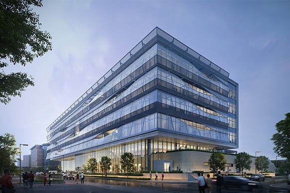 A glass-fronted office building featuring multiple floors, landscaped greenery, and people walking outside during twilight hours.