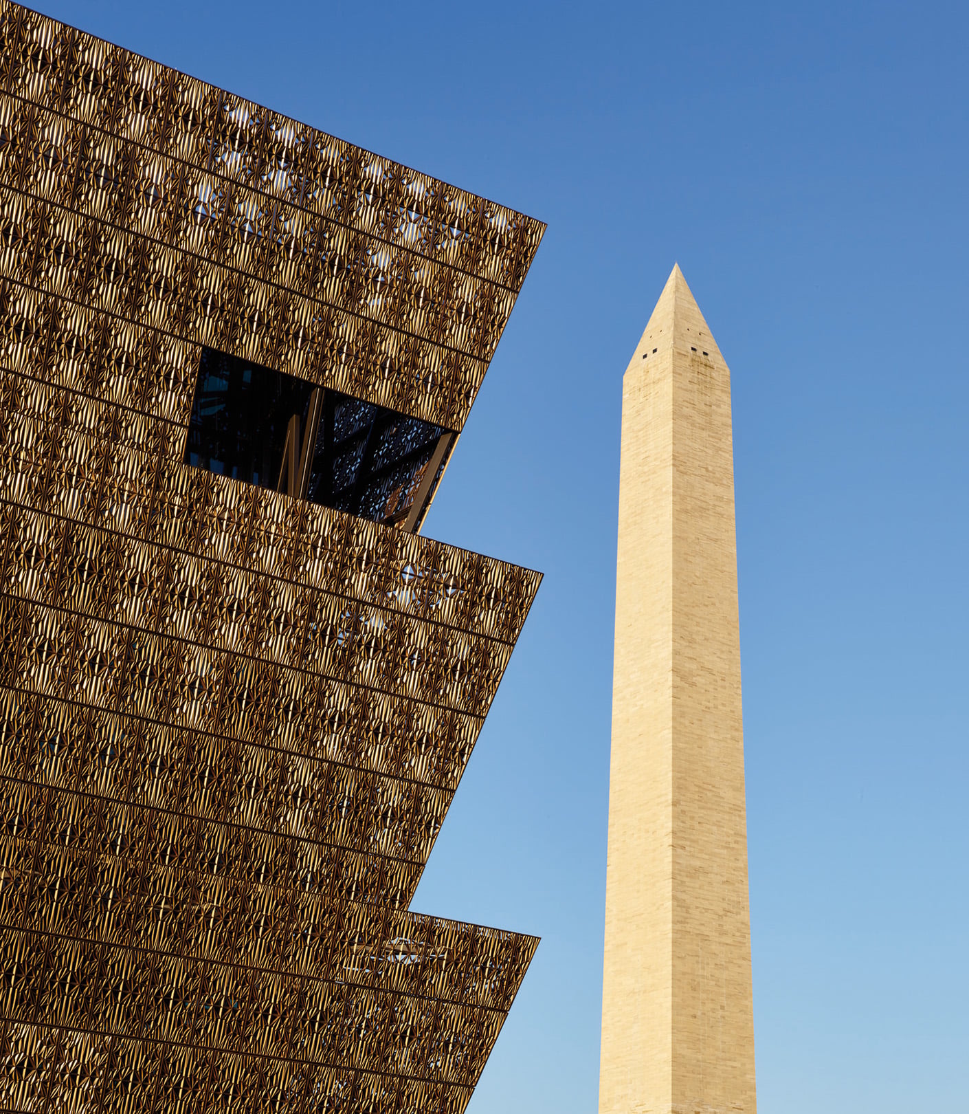 Smithsonian National Museum of African American History and Culture with Washington Monument in background against blue sky.