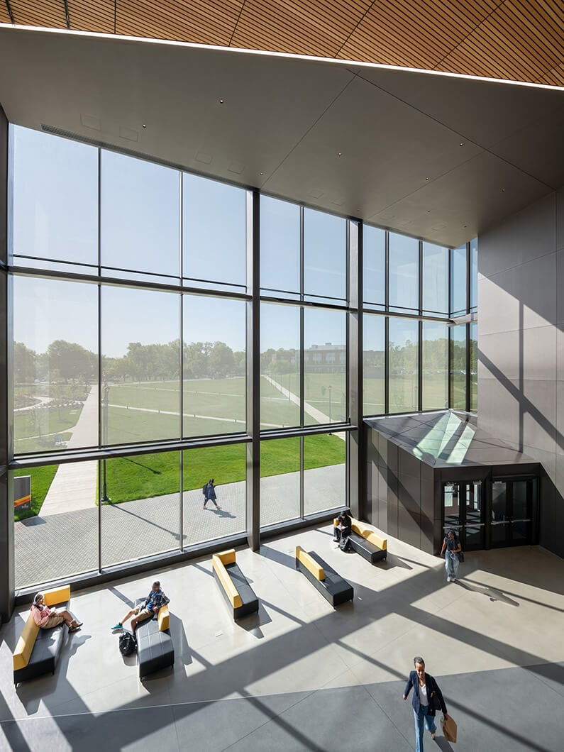 Bright, spacious lobby with large windows and sleek seating. People engage in various activities, showing a lively indoor atmosphere.