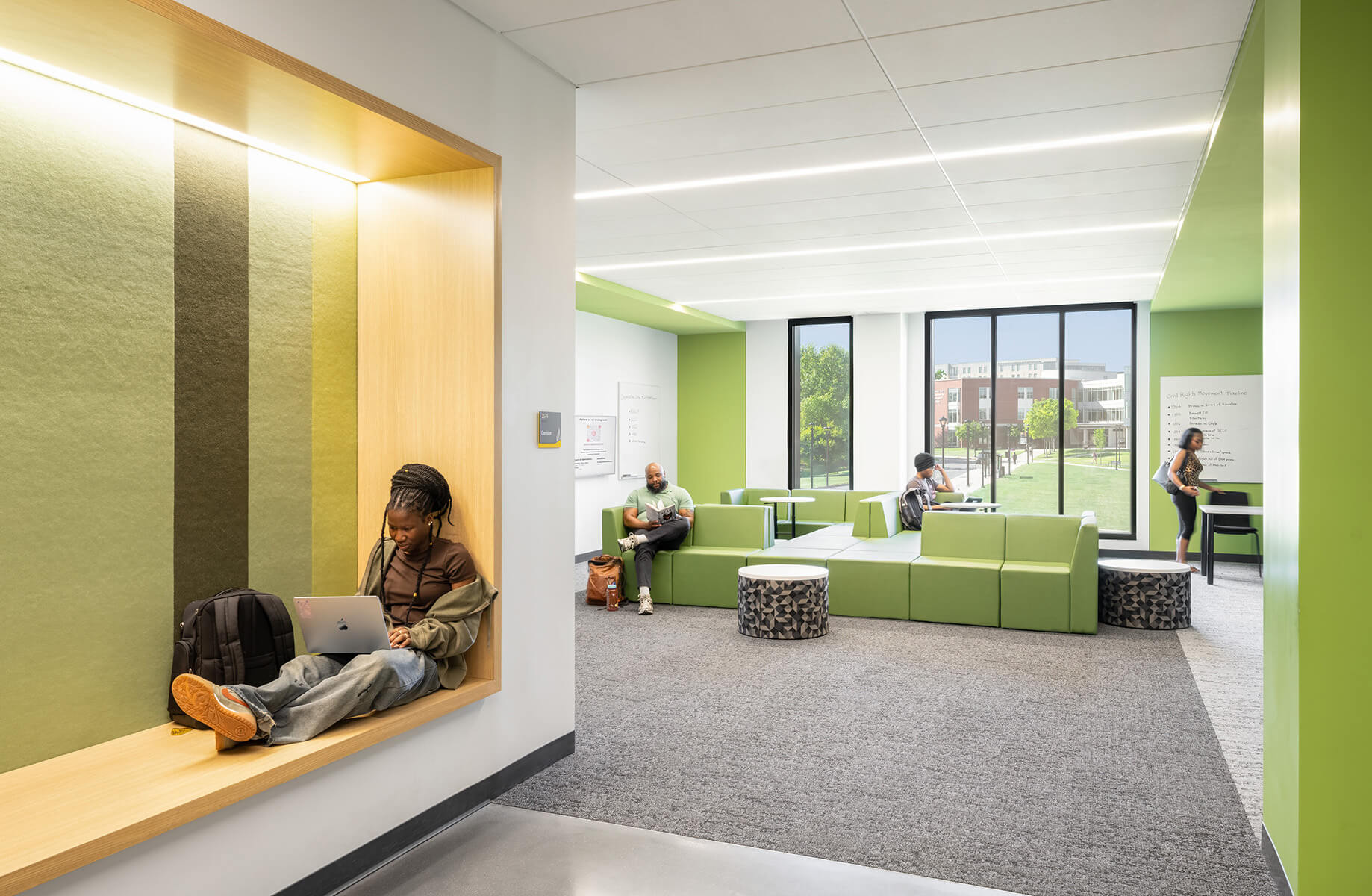 Students work and relax in a spacious area featuring soft seating and natural light, with green walls and modern furnishings.