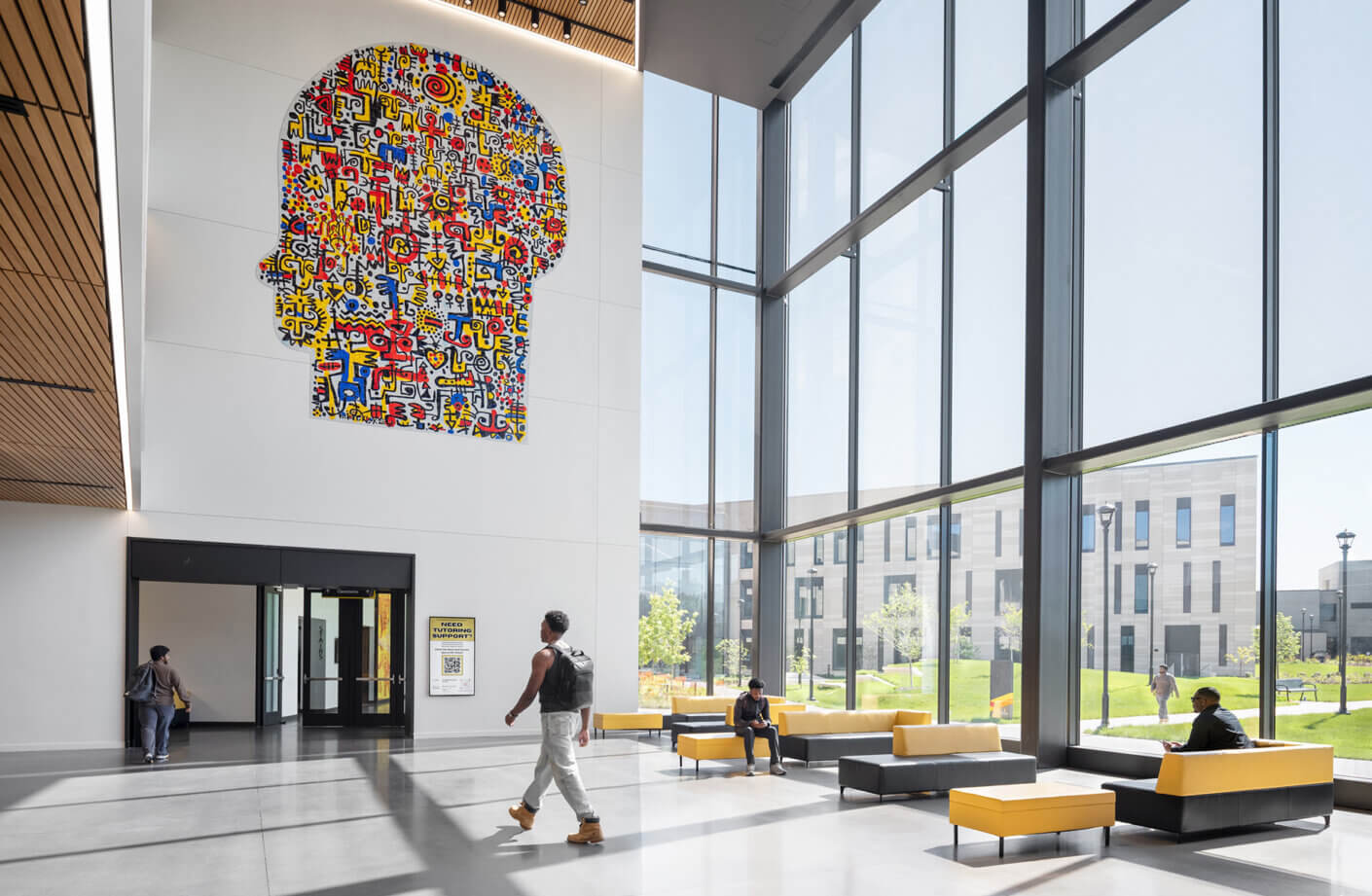 Bright lobby featuring large graphic mural of a head silhouette, large windows, and diverse seating areas with yellow and gray couches.