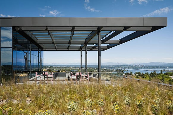 Rooftop terrace with glass walls and a covered seating area overlooking a landscape with greenery and distant mountains.