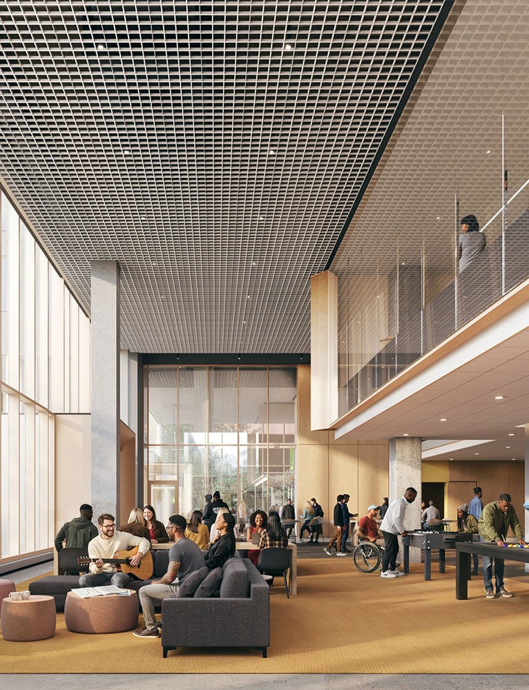 Interior view of a spacious communal area with people socializing, playing games, and relaxing on sofas under a grid ceiling and large windows.