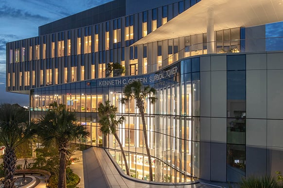 Exterior view of the Kenneth C. Griffin Surgical Tower at dusk, featuring glass architecture and landscaped palm trees.