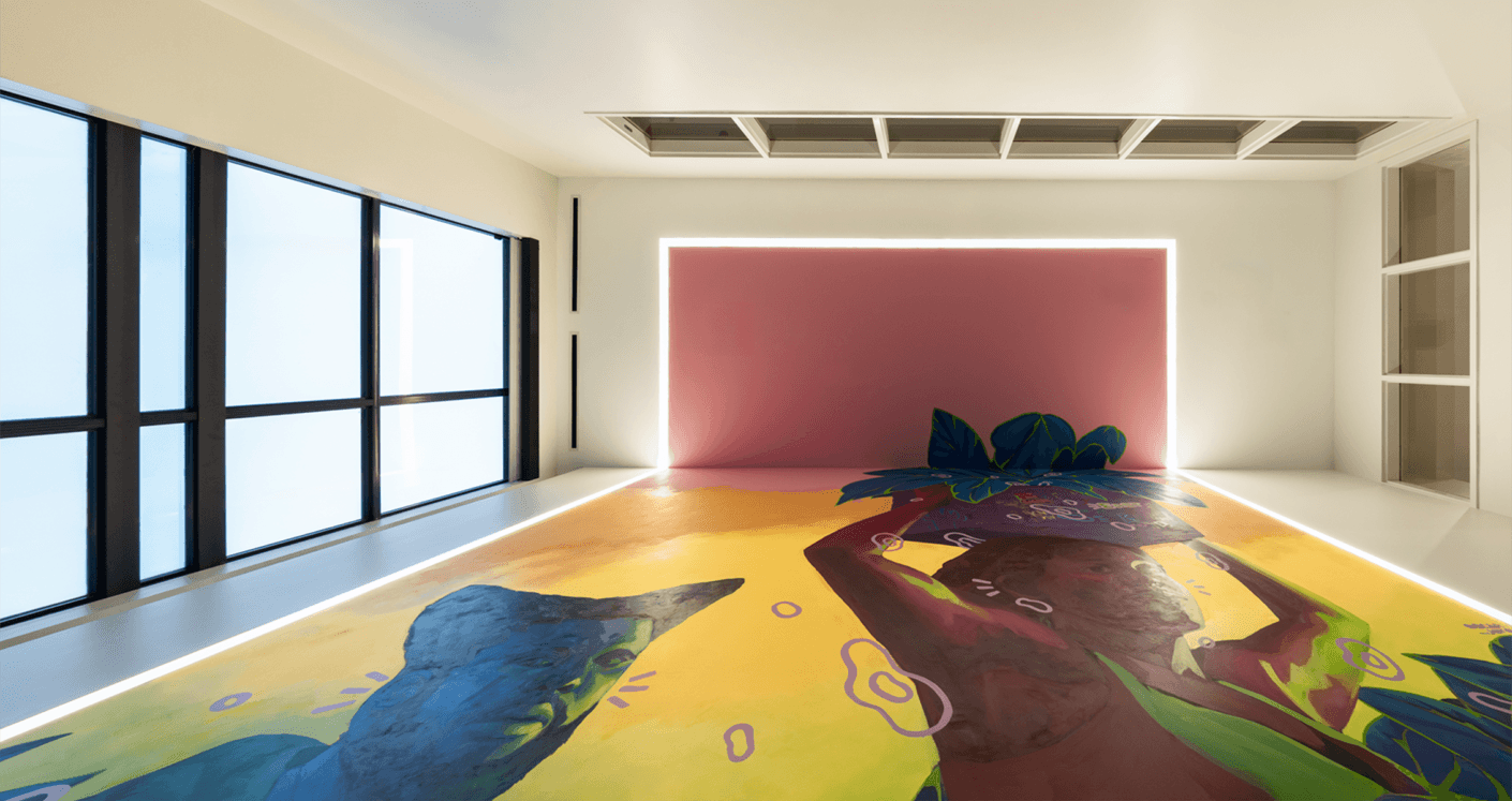 Interior space featuring large windows, a pink wall, and vibrant floor art depicting figures and plants with colorful designs.