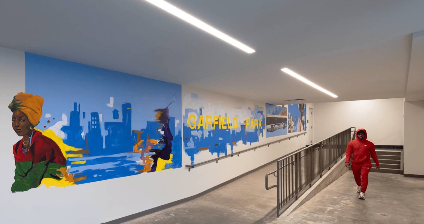 A person wearing a red outfit walks through a stairwell featuring vibrant murals of Garfield Park and urban scenes.