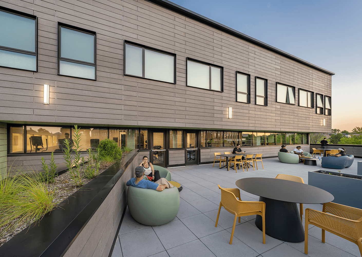 A rooftop terrace features seating areas with a mix of bean bags and tables, with people enjoying the outdoor space and greenery.
