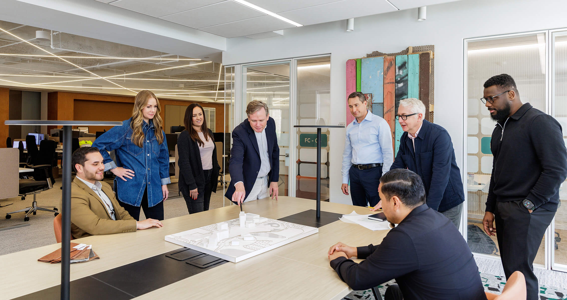 Group of professionals collaborating around a table with a layout model, discussing plans in a well-lit office environment.