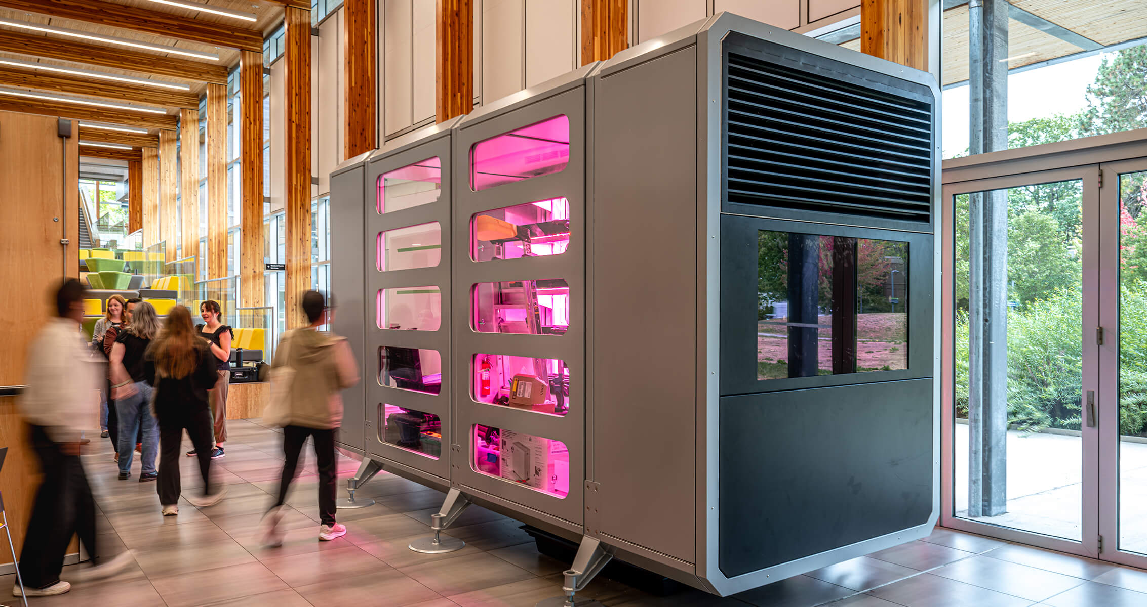 Interior view of a space featuring a sleek, multi-functional unit with pink lighting, surrounded by people engaging in conversation.