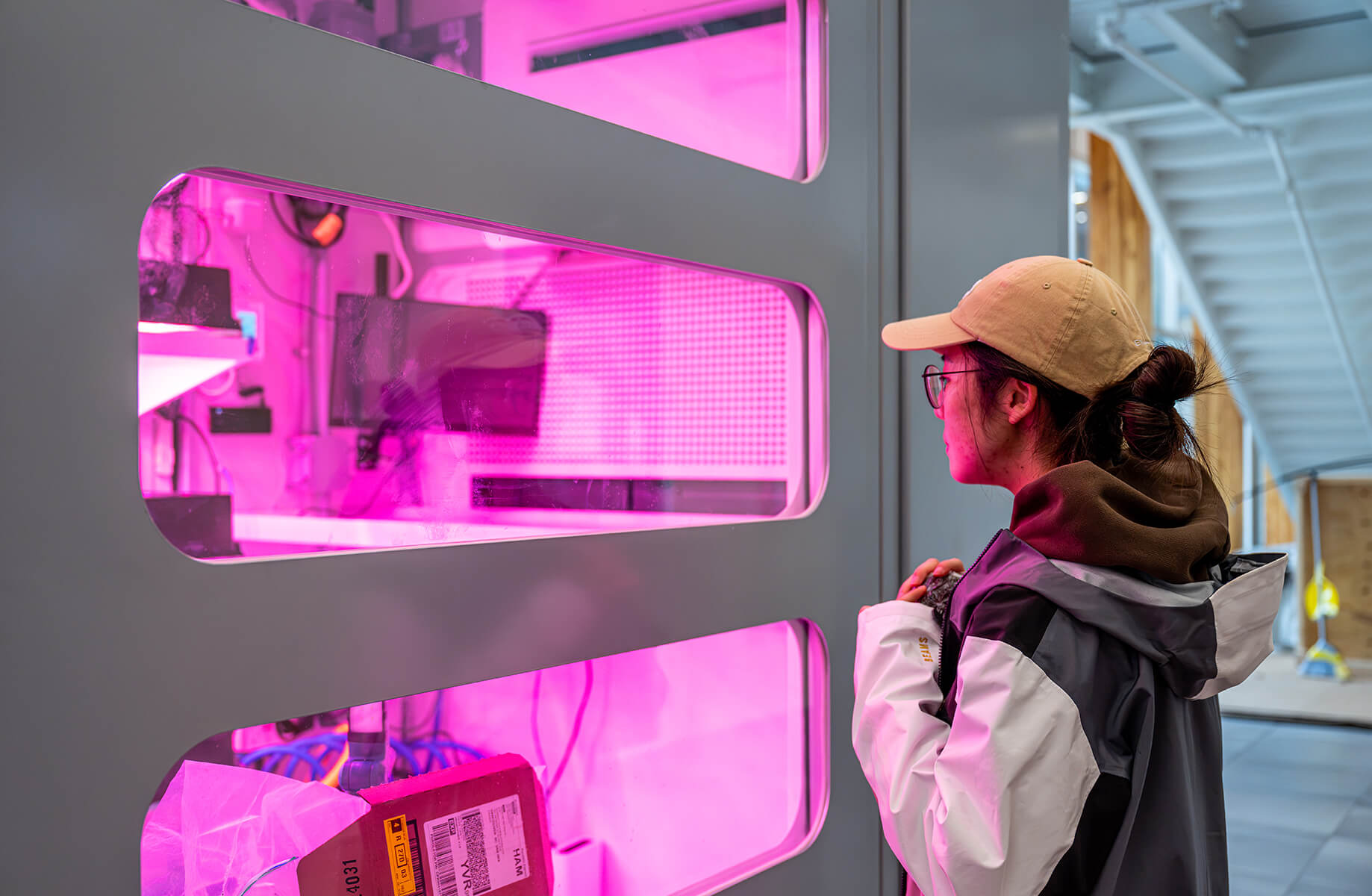 A person in a cap observes a display with pink lighting and technology, showcasing a high-tech environment focused on innovation.