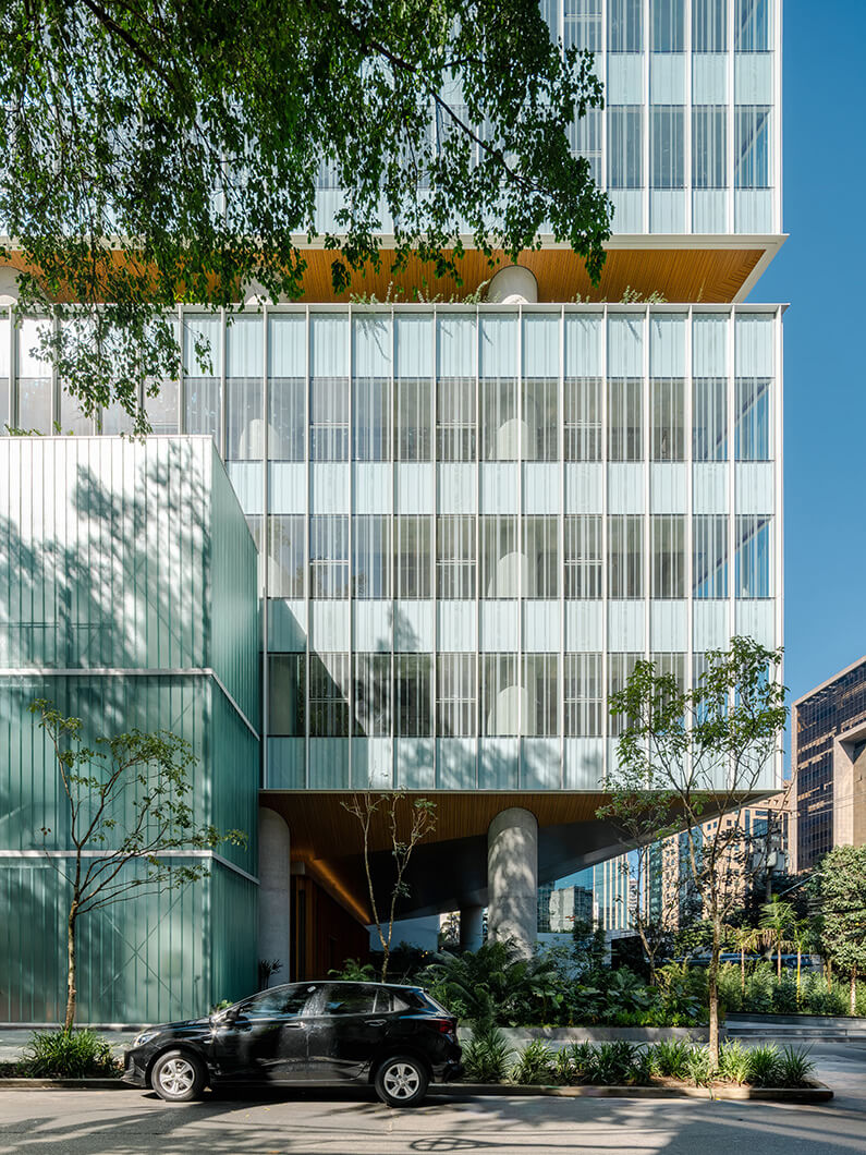 Exterior view of a glass and concrete building with greenery and a parked black SUV in the foreground, showcasing urban architectural design.