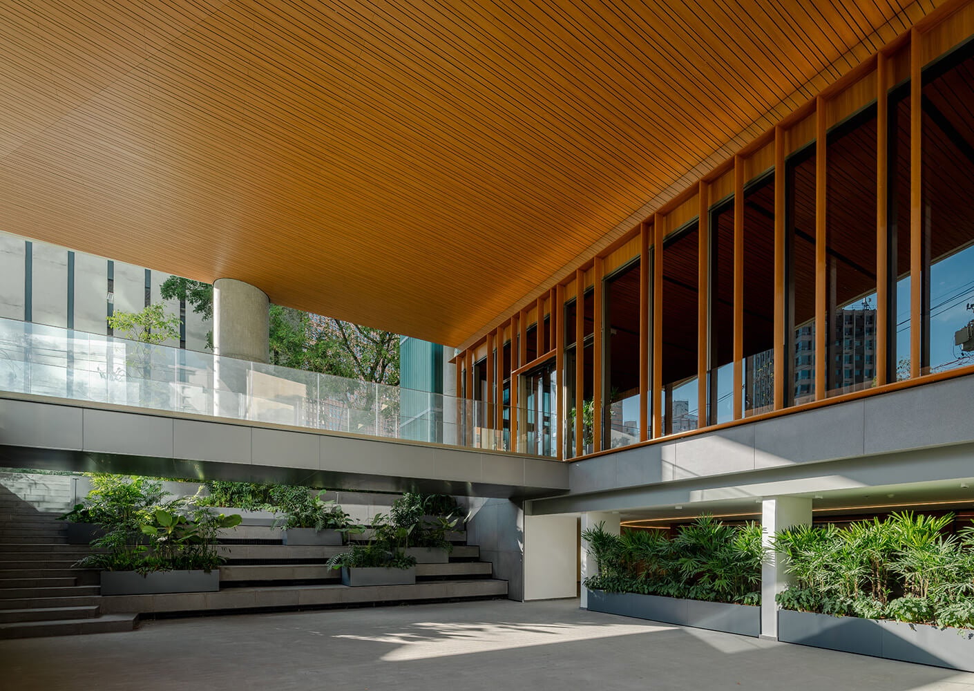 Interior space featuring wooden ceiling, large glass windows, and greenery. Stairs lead down to a landscaped area. Natural light enhances the atmosphere.