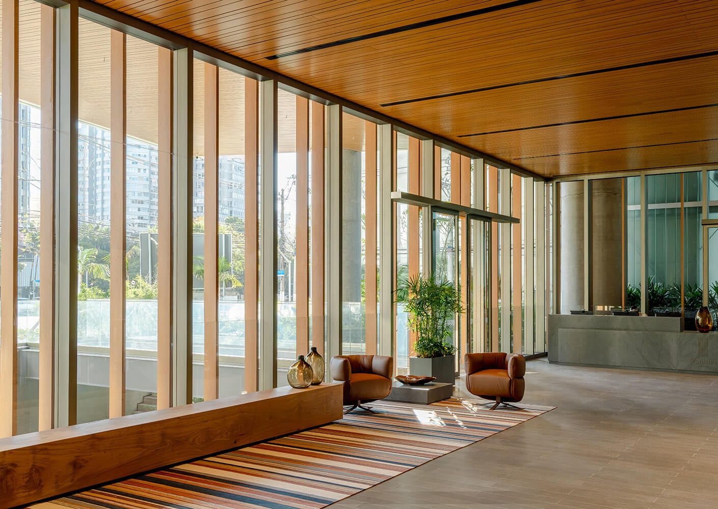 Interior view of a spacious lobby featuring large windows, wooden ceiling, and contemporary seating area with plants and decorative elements.