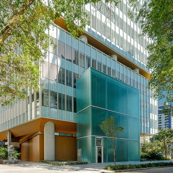 Glass and wooden building corner with a turquoise accent, surrounded by trees and landscaping in an urban setting.
