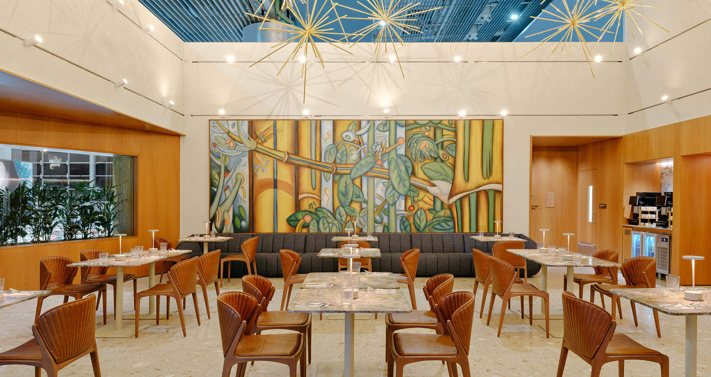 Interior of a restaurant featuring wooden elements, artistic wall mural, stylish seating, and modern lighting fixtures. Tables set for dining.