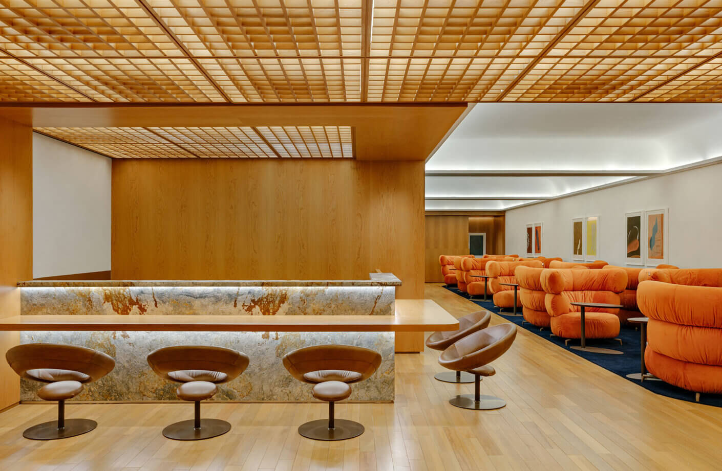 Creative lounge area featuring a wood-paneled bar, sculptural seating, and warm lighting, complemented by orange cushioned chairs.