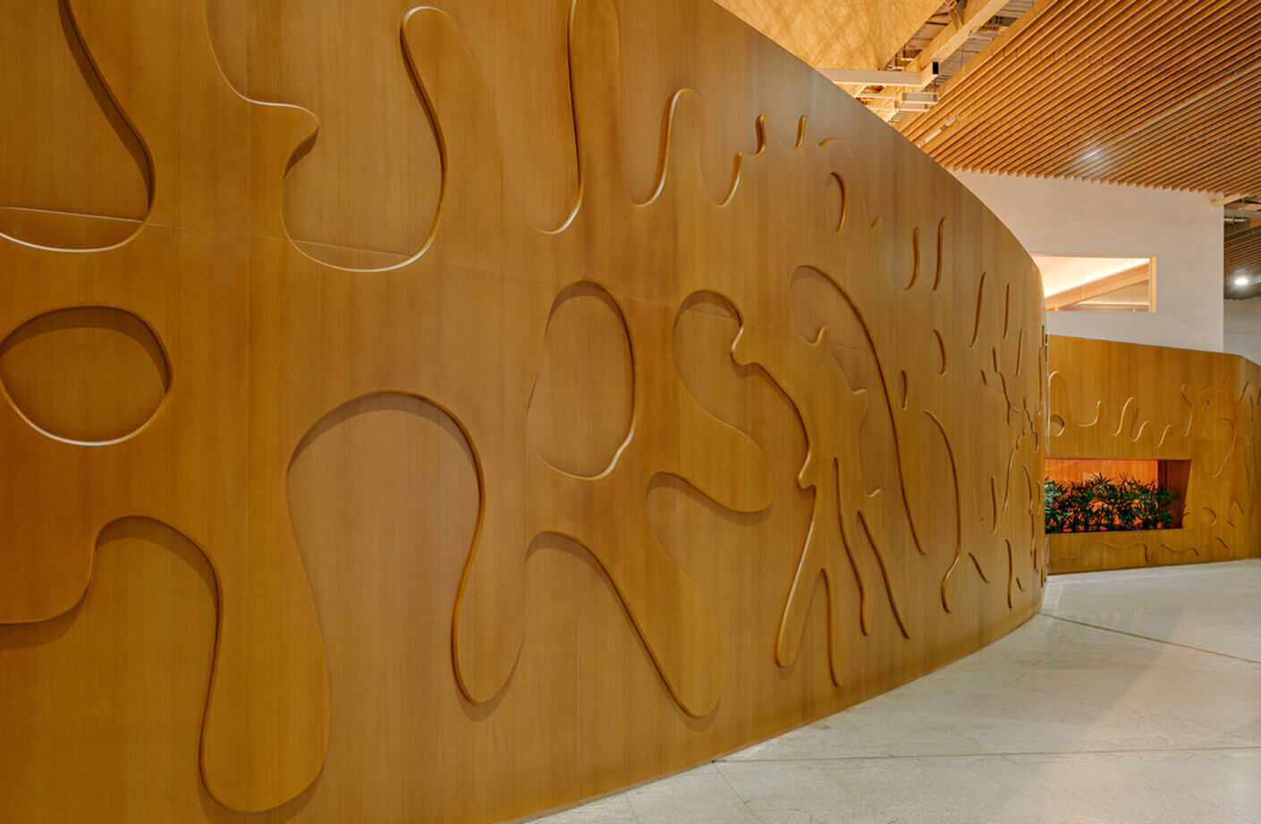 Wooden wall with abstract cutouts and patterns, featuring a curved design and integrated planter for greenery. Ideal for architectural spaces.