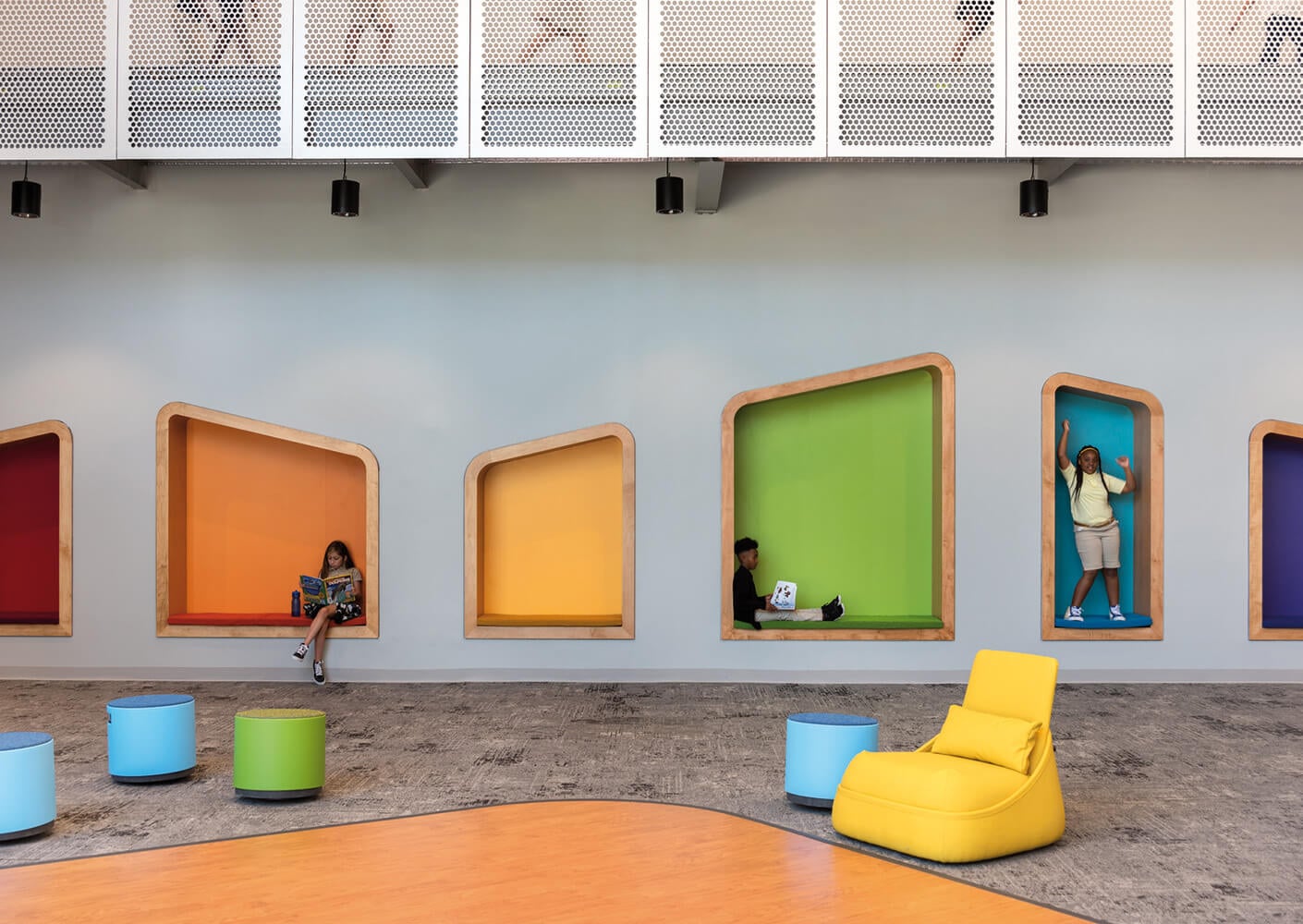 Colorful interior space with unique alcoves, featuring children engaged in reading and play. Bright seating and textured flooring enhance the design.