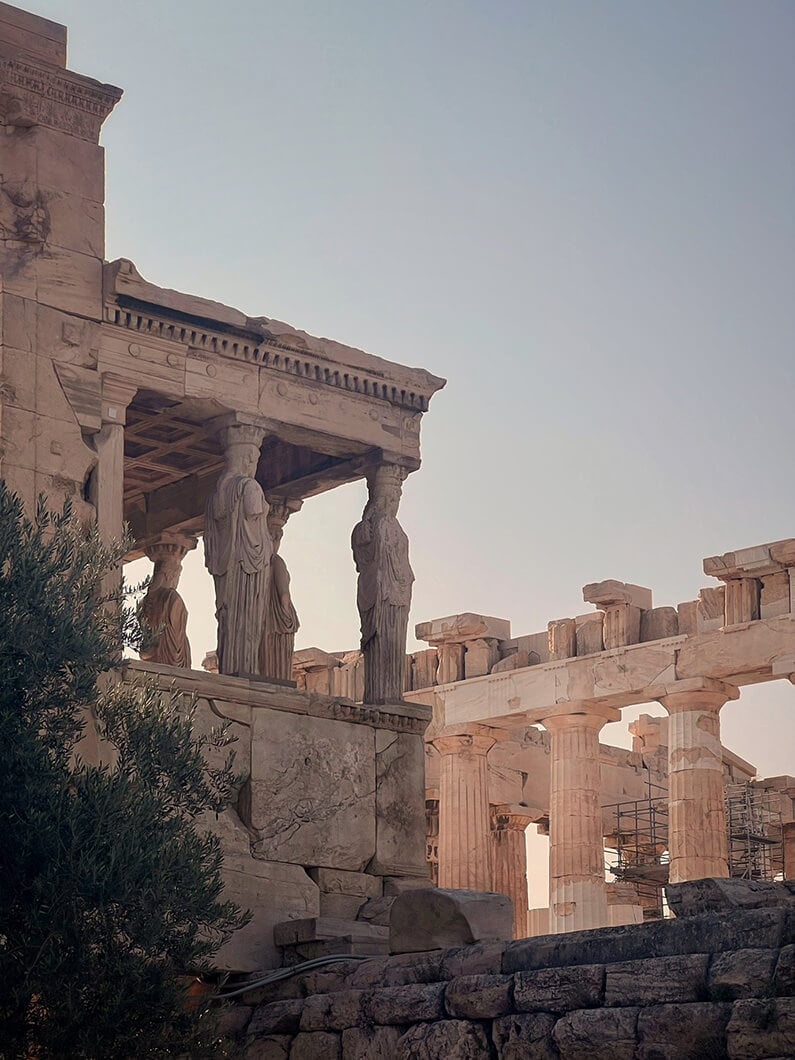 Caryatids support the porch of the Erechtheion, with the Parthenon in the background and scaffoldings visible, at the Acropolis of Athens.