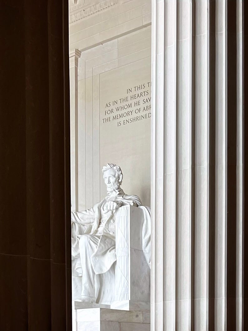 Lincoln Memorial statue of Abraham Lincoln, seated, surrounded by columns. Inscription visible on the wall behind him.