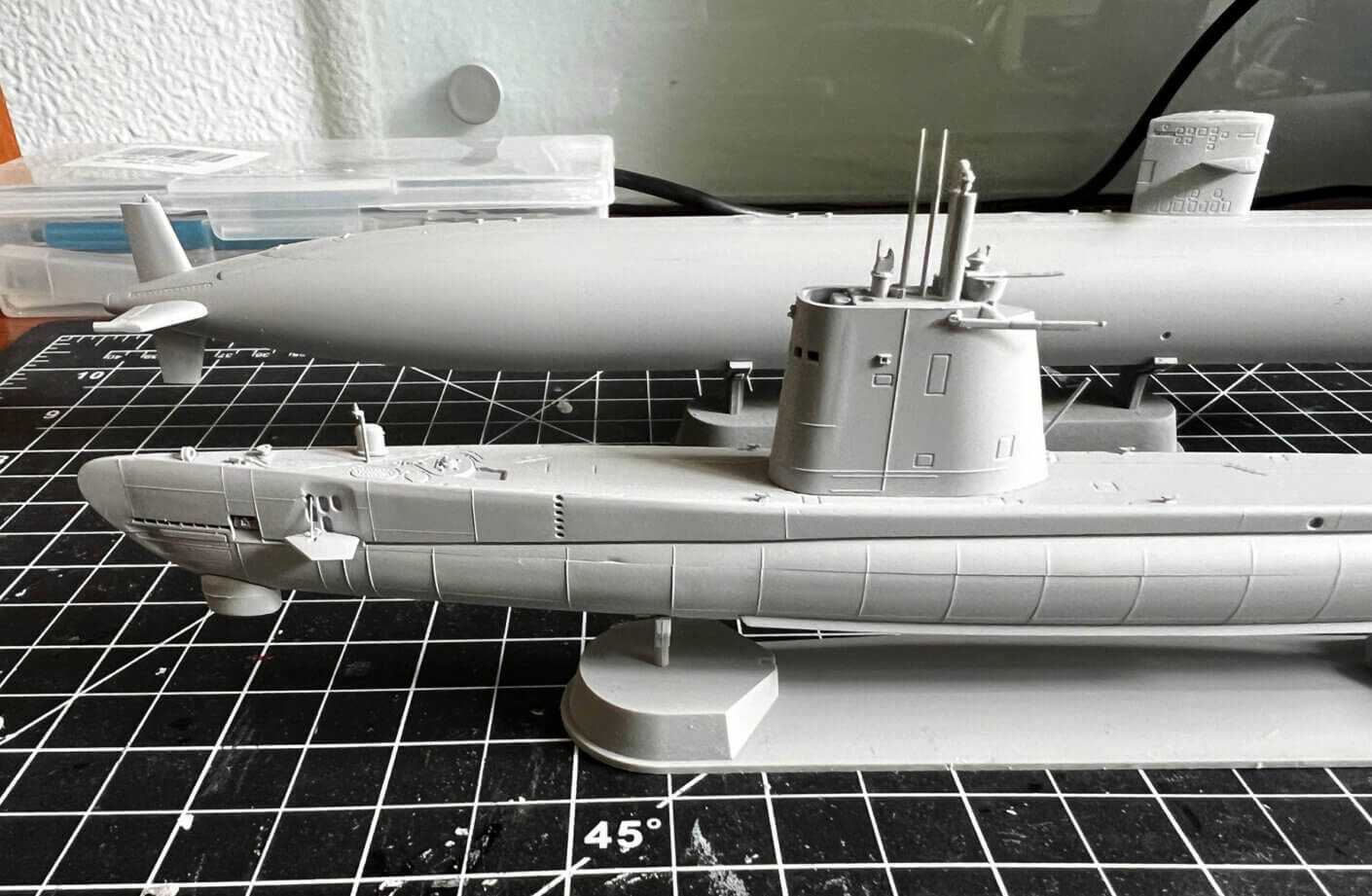A close-up of two gray submarine models on a grid cutting mat, showcasing detailed features and design elements.